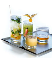 Vier verschiedene Gläser auf einem Tablett, darunter ein Whiskyglas, aus der Vogelperspektive fotografiert.