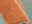 Nahaufnahme eines orangefarbenen Frisé-Teppichs mit einer weißen Linie, aufgerollt auf einem grünlichen Hintergrund.