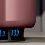 Nahaufnahme eines rosafarbenen Schmortopfs auf einem Gasherd mit blauer Flamme.