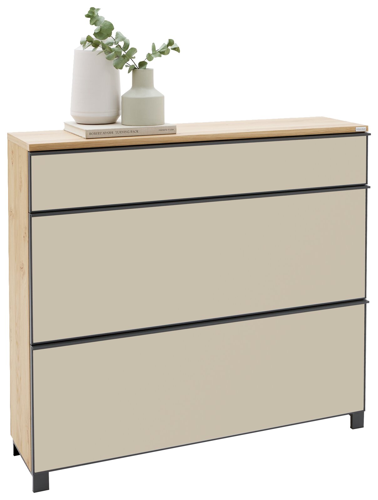 Moderne Kommode mit drei grifflosen Schubladen, beige Fronten mit dunklen Kanten und Holzrahmen, auf der Deckplatte zwei Vasen mit Eukalyptus; frontale Ansicht leicht von links auf weißem Hintergrund.