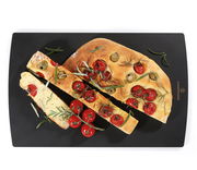 Schwarzes Schneidbrett 36x23cm mit geschnittenem Focaccia-Brot, Tomaten und Rosmarin, aus der Vogelperspektive.