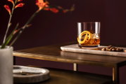 Whiskyglas mit Eiswürfeln und Orangenschale auf einem Tisch, seitliche Perspektive
