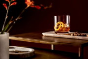 Whiskyglas mit Eiswürfeln und Orangenschale auf einem Tisch, seitliche Perspektive