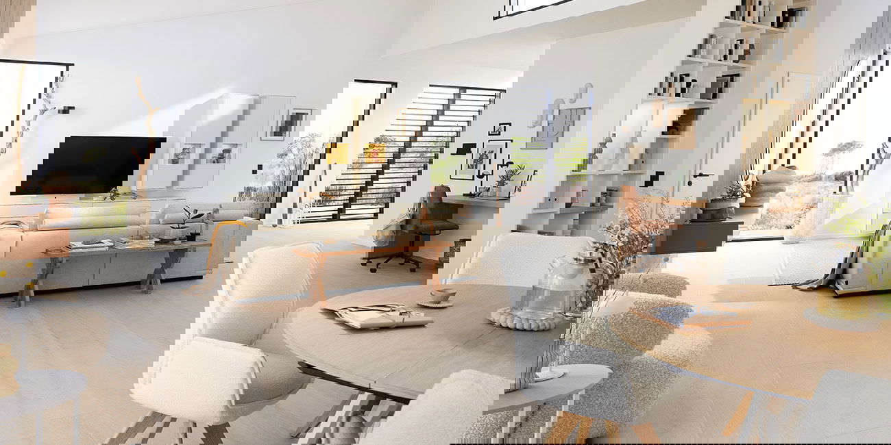 Das Wohnzimmer ist hell und modern eingerichtet. Ein großes Sofa lädt zum Entspannen ein. Es gibt einen Fernseher und viel Platz. Ein Esstisch mit Stühlen steht im Raum, ideal für Mahlzeiten. Helle Möbel und große Fenster lassen den Raum freundlich wirken