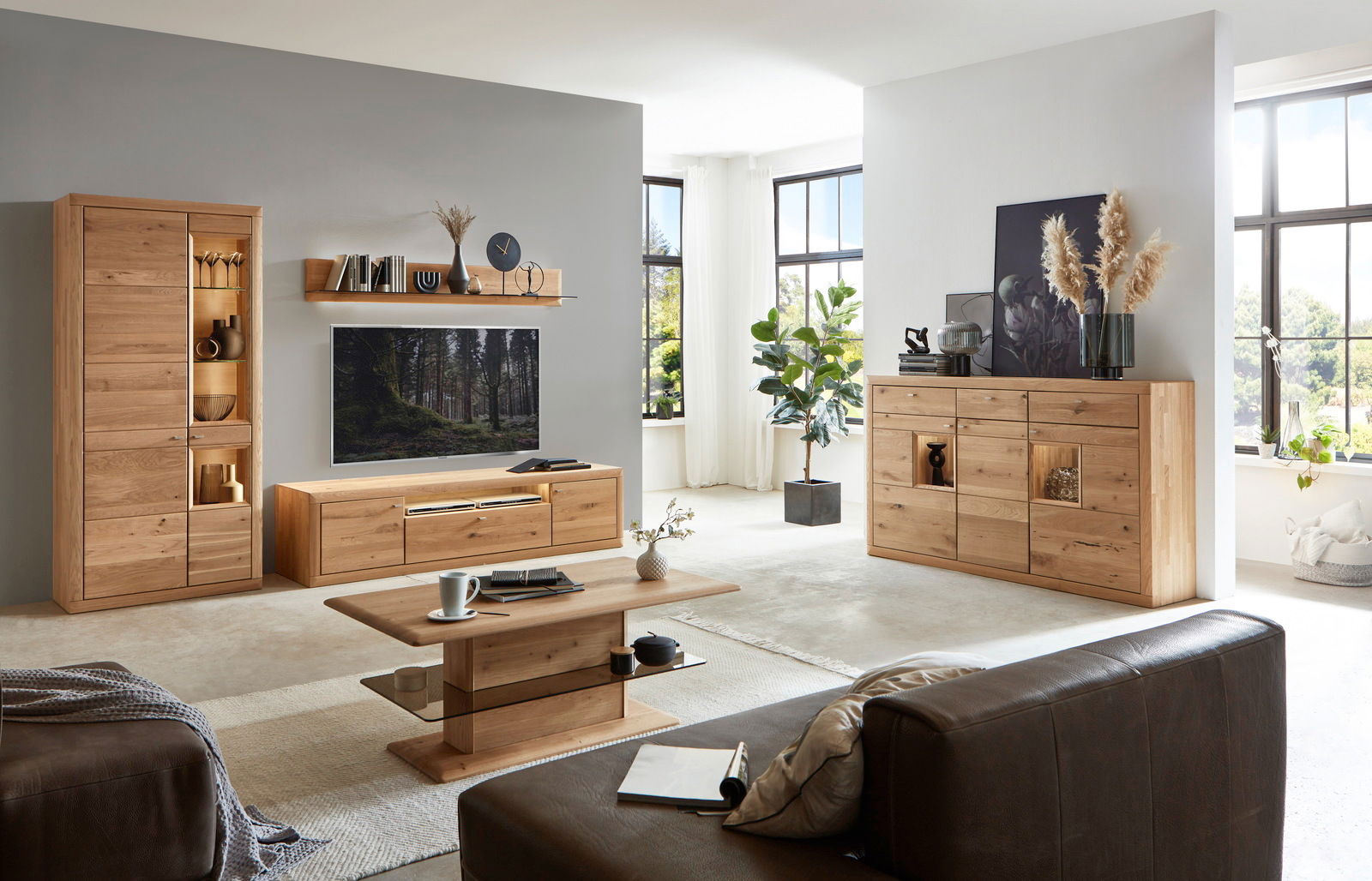 Wohnzimmer mit moderner Wandkombination aus Holz, bestehend aus Vitrine, TV-Board und Regal, im Vordergrund ein Couchtisch, seitliche Perspektive.