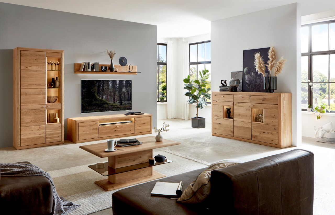 Wöstmann Markenmöbel Highboard AURUM Wohnzimmer mit moderner Wandkombination aus Holz, bestehend aus Vitrine, TV-Board und Regal, im Vordergrund ein Couchtisch, seitliche Perspektive.