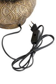 Nahaufnahme einer Tischleuchte mit kunstvoll verziertem, goldfarbenem Lampenschirm und schwarzem Kabel mit Schalter, seitliche Perspektive.