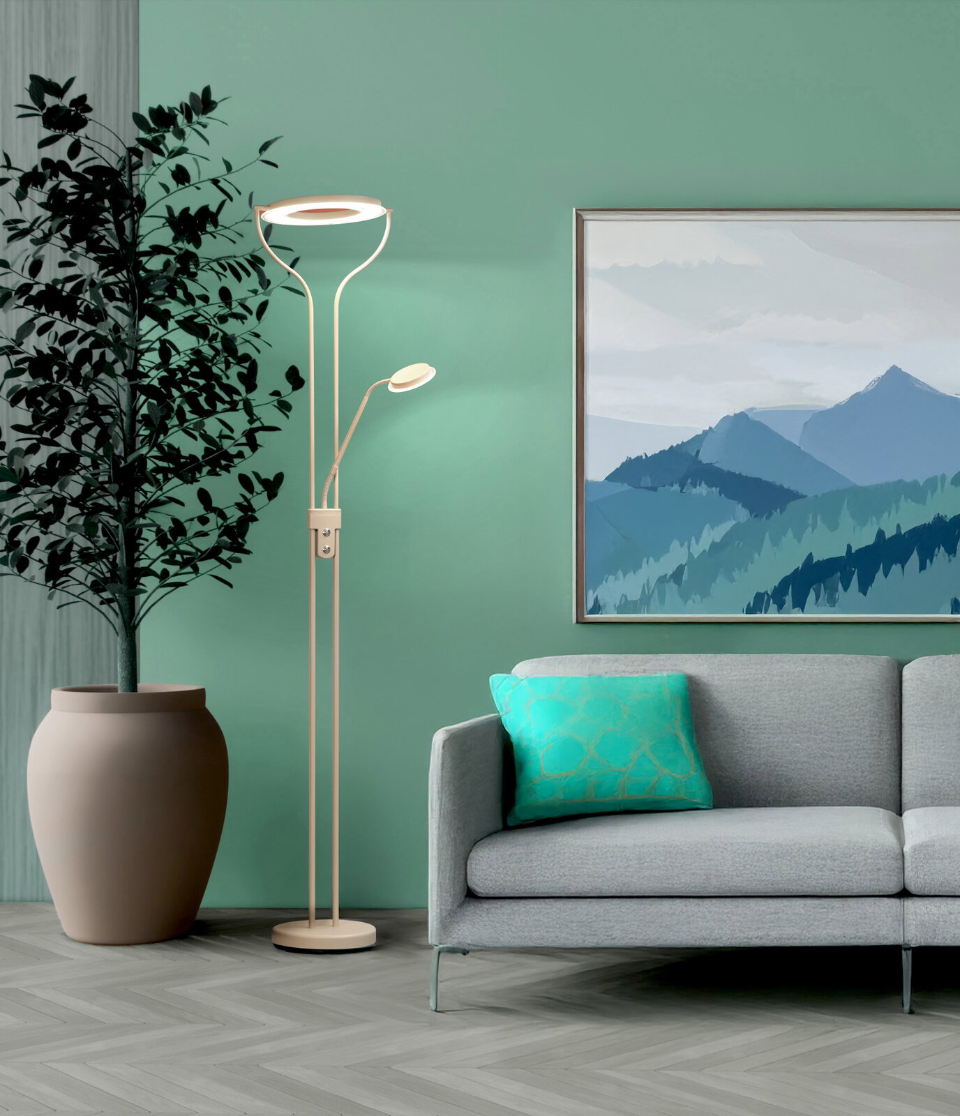 Moderne LED-Stehlampe in Beige/Champagner mit Ring-Deckenfluter und kleinem Lesearm, frontal in einem Wohnzimmer neben grauem Sofa und großer Pflanze vor grüner Wand.