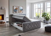 Graues Boxspringbett BX2200 CHESTER mit Stauraumfunktion, seitliche Perspektive, in modernem Schlafzimmer mit Kamin und großen Fenstern.