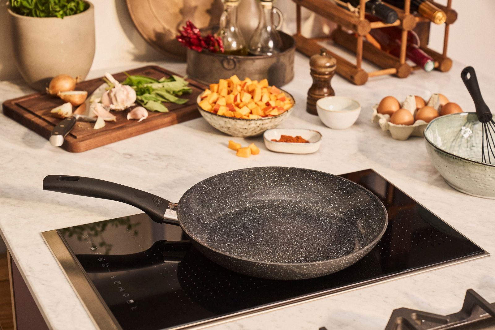 Bratpfanne mit 24 cm Durchmesser auf einem Induktionskochfeld, umgeben von frischen Zutaten in einer modernen Küche, aus der Vogelperspektive.