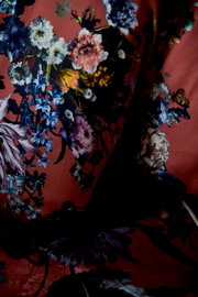 Nahaufnahme aus frontaler Perspektive auf einen drapierten Stoff mit opulentem Blumenmuster in Blau, Weiß, Rosa und Violett auf dunkelrotem Grund.