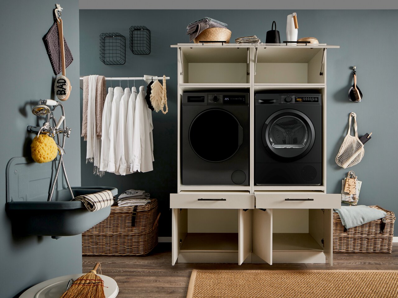 Frontale Perspektive: moderner Waschturm/Waschmaschinen-Schrank in Weiß mit zwei schwarzen Frontlader-Geräten (Waschmaschine und Trockner) in einem stilvollen Hauswirtschaftsraum, mit offenen Schranktüren unten und Ablagefläche oben.