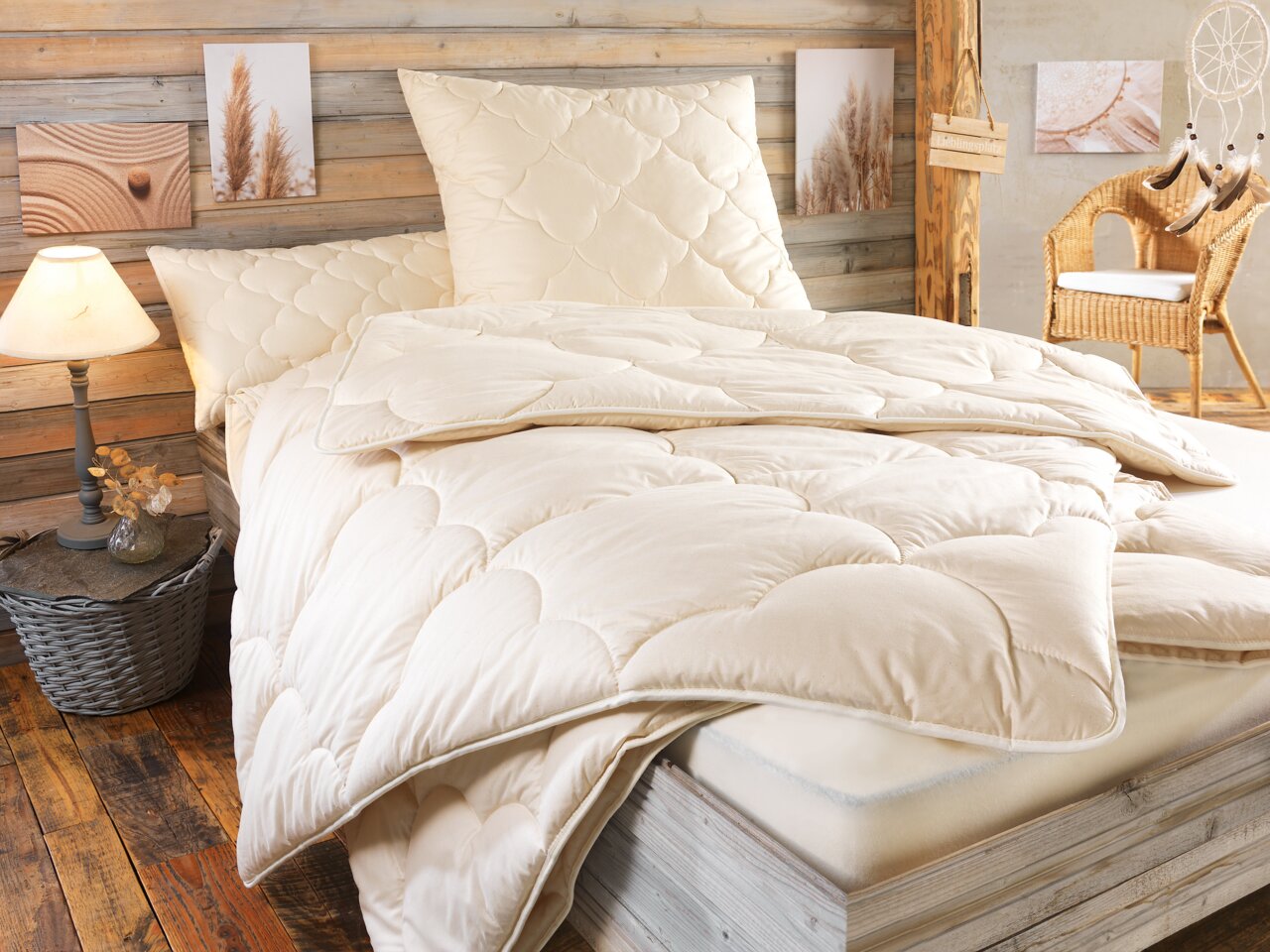 Valnatura Steppbett HANF RELAX Gemütliches Schlafzimmer mit einem beigen Steppbett auf einem Holzrahmenbett, umgeben von rustikaler Dekoration. Perspektive von der Seite des Bettes.