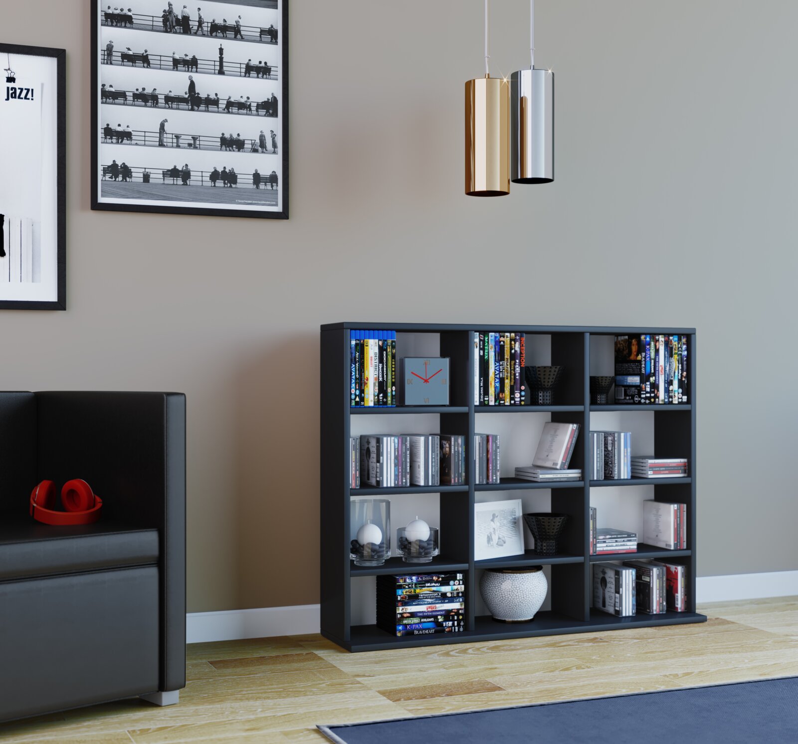 Frontale Innenraumansicht eines modernen Wohnzimmers: schwarzes Regal mit Büchern und Deko, darüber zwei zylindrische Pendelleuchten in Gold und Silber vor grauer Wand