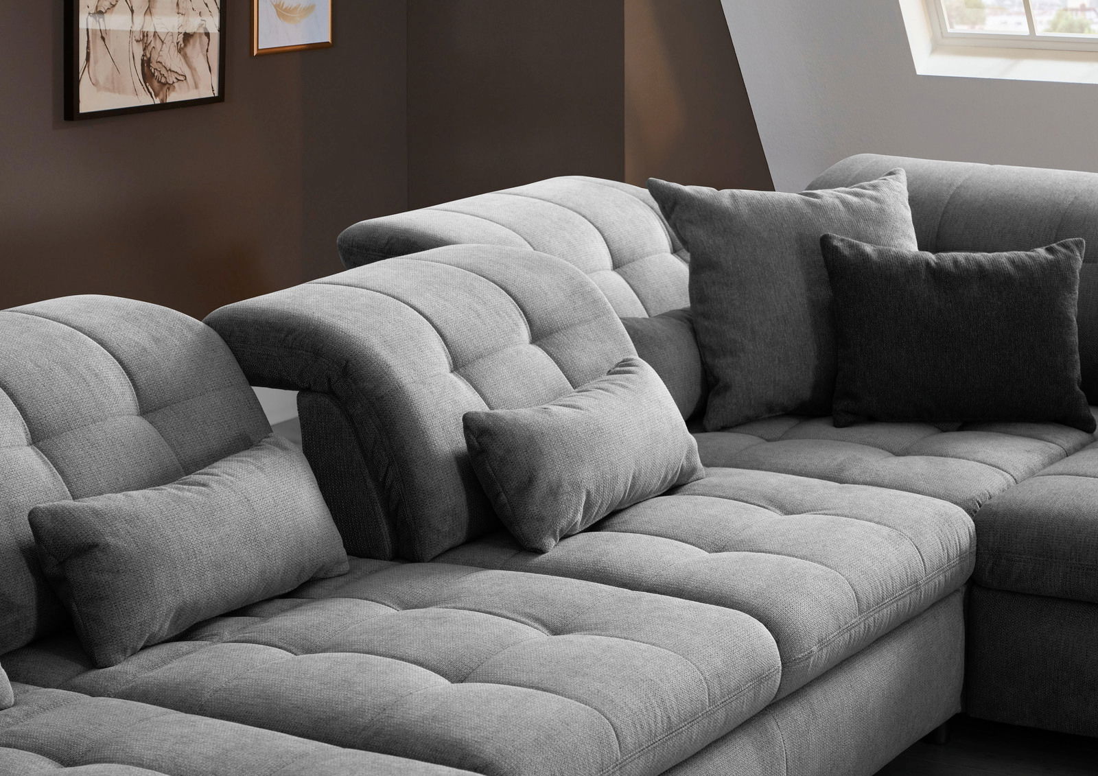 Graues, modernes Sofa mit verstellbaren Kopfstützen und mehreren Kissen, seitliche Perspektive.