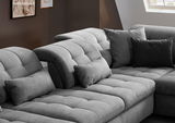 Graues, modernes Sofa mit verstellbaren Kopfstützen und mehreren Kissen, seitliche Perspektive.