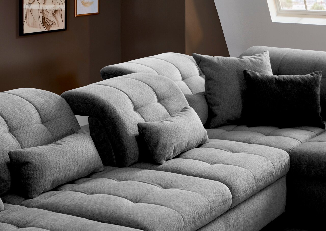 Graues, modernes Sofa mit verstellbaren Kopfstützen und mehreren Kissen, seitliche Perspektive.