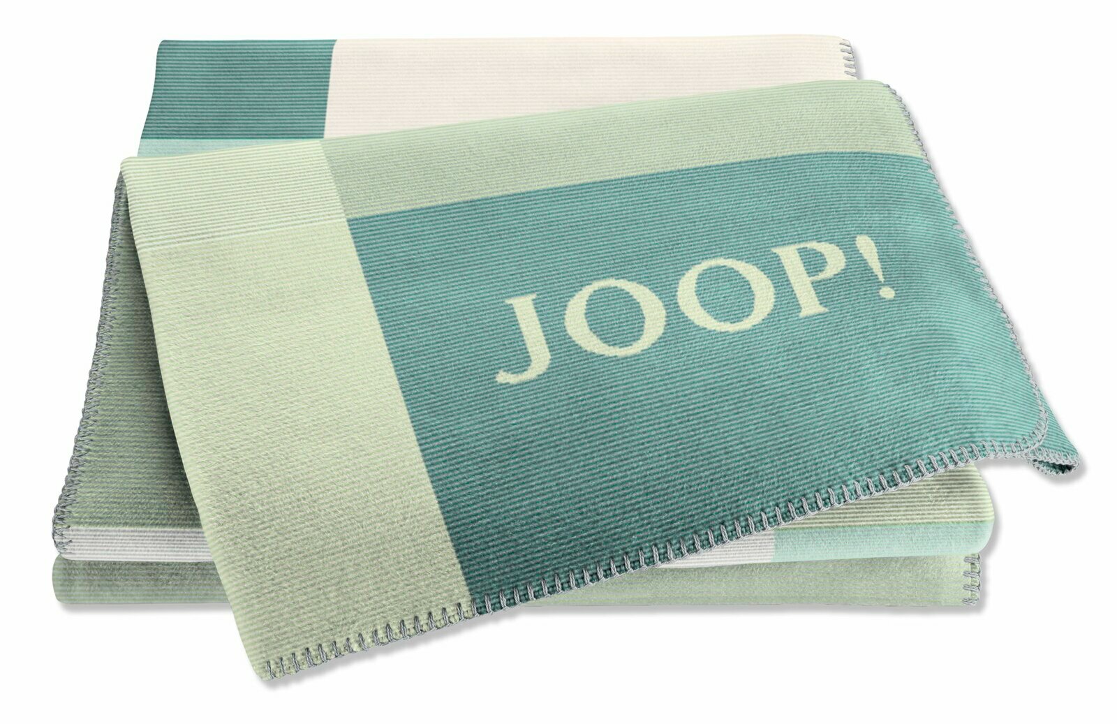 Gefaltete Wohndecke in Grün- und Blautönen mit dem Schriftzug 'JOOP!' in der Mitte, aus einer leicht schrägen Perspektive fotografiert.
