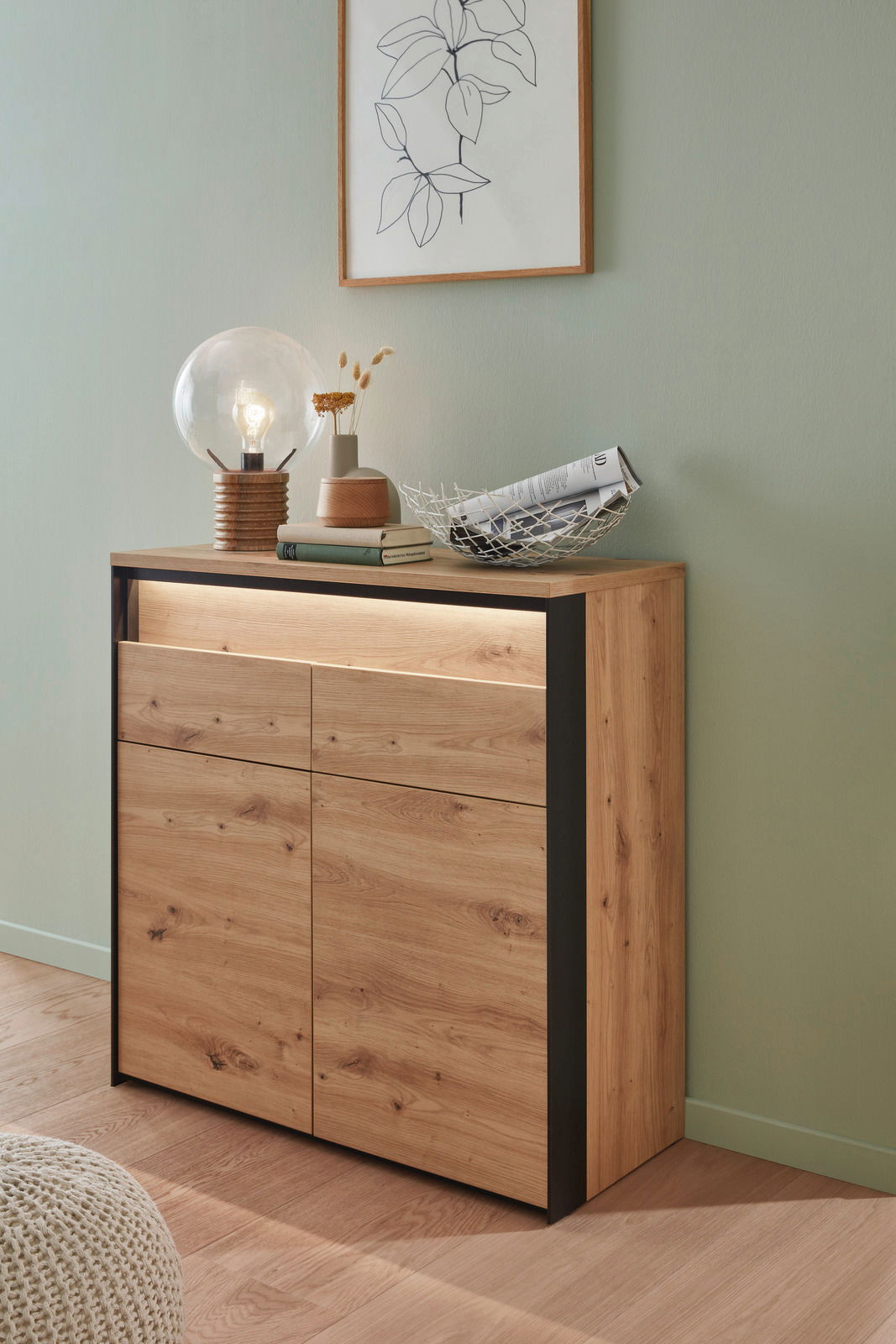 Moderne Kommode aus Holz mit schwarzem Rahmen, dekoriert mit einer Lampe, Büchern und einer Schale, seitliche Perspektive.