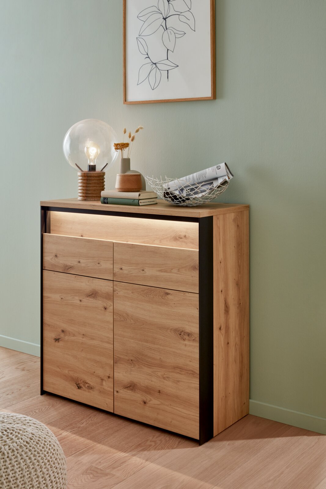 Moderne houten ladekast met zwart frame, versierd met een lamp, boeken en een schaal, gezien vanuit de zijkant.