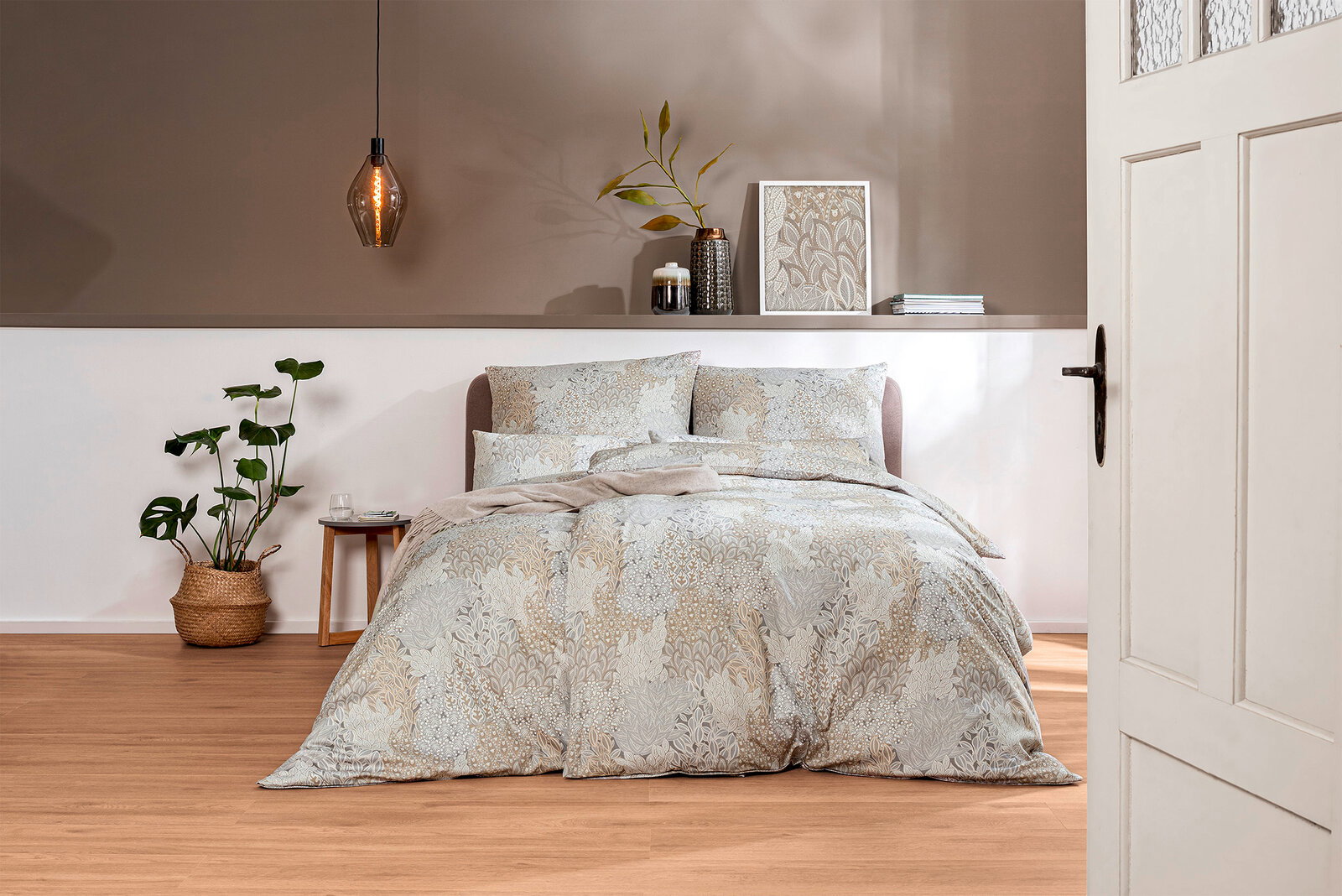Bettwäsche-Set in einem stilvollen Schlafzimmer mit Pflanzen und moderner Dekoration, aus der Perspektive durch eine geöffnete Tür betrachtet.