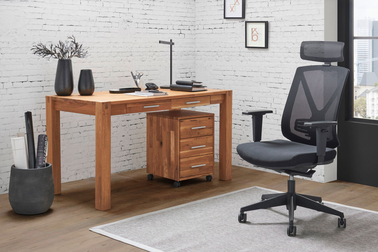 Moderner Schreibtisch aus Holz mit Schubladen, seitliche Perspektive, neben einem ergonomischen Bürostuhl in einem stilvollen Büro mit weißer Backsteinwand.