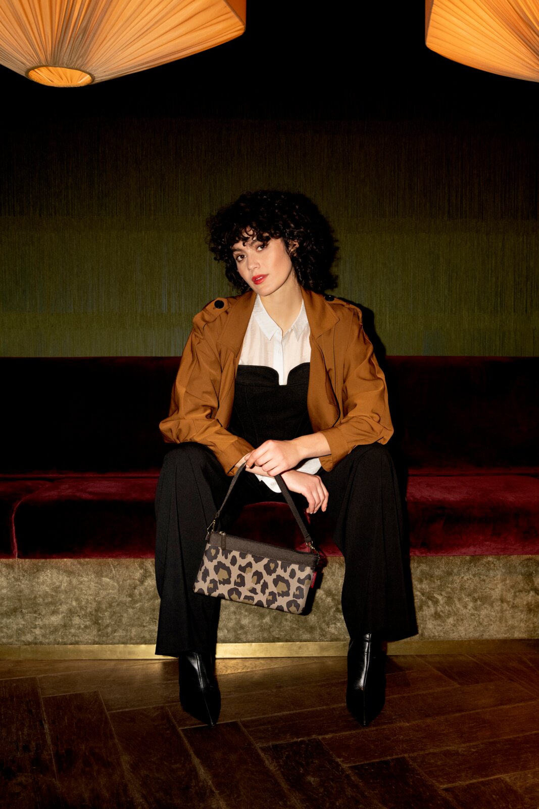 Frau sitzt auf einem Sofa und hält eine Mini-Tasche mit Leopardenmuster in der Hand, frontale Perspektive.