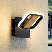 Moderne LED-Wandleuchte in Schwarz mit rechteckigem Leuchtring und Holzsteg, warmweiß leuchtend an strukturierter Wand, schräg von vorne in Nahaufnahme fotografiert