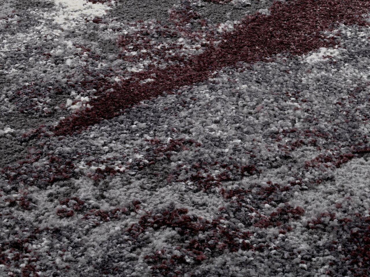 Nahaufnahme eines Teppichs mit abstraktem Muster in Grau- und Rottönen, perspektivisch von schräg oben betrachtet.