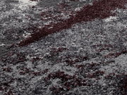 Nahaufnahme eines Teppichs mit abstraktem Muster in Grau- und Rottönen, perspektivisch von schräg oben betrachtet.