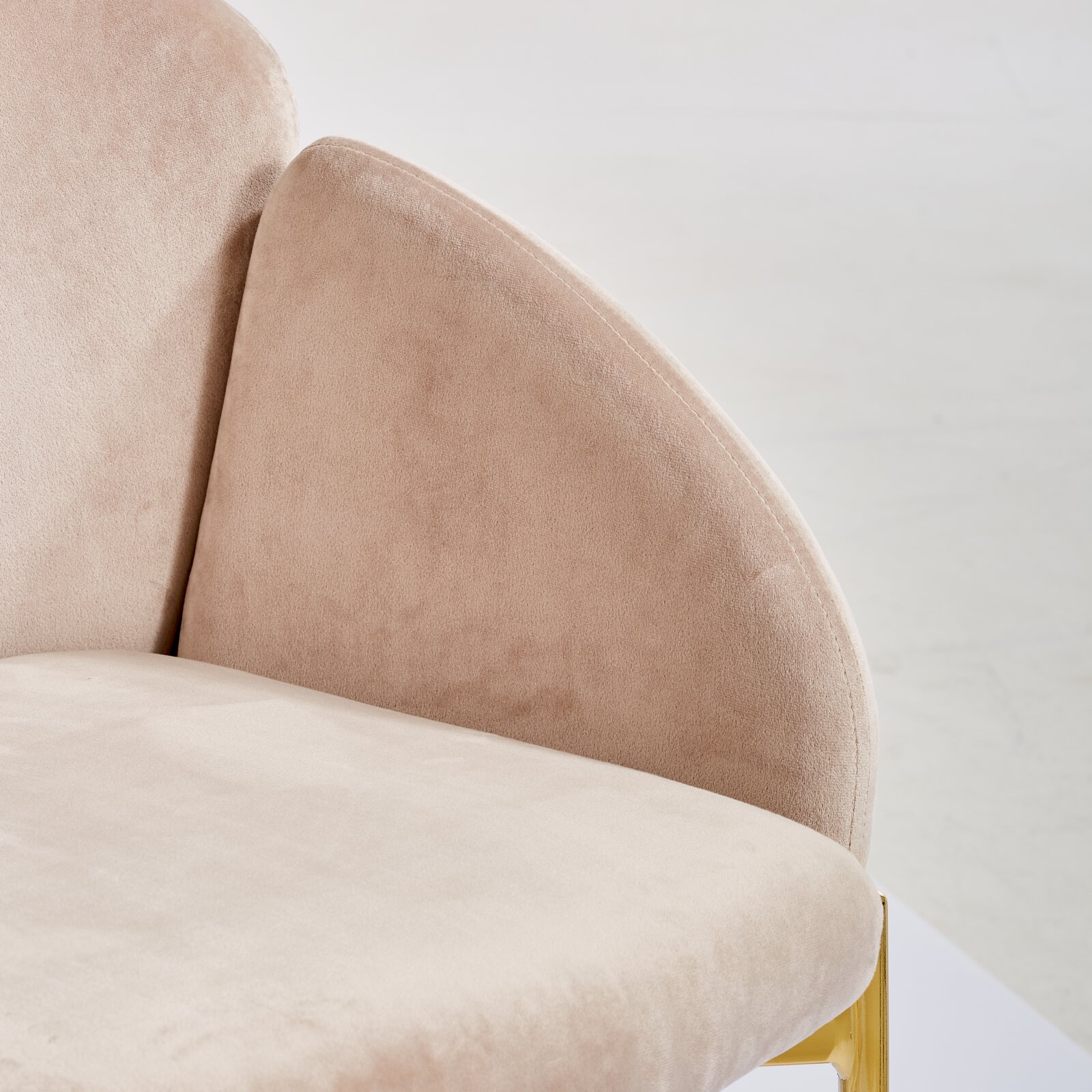 Close-up van een beige fauteuil met een fluweelachtig oppervlak en gouden accenten, gezien vanaf de zijkant
