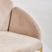 Close-up van een beige fauteuil met een fluweelachtig oppervlak en gouden accenten, gezien vanaf de zijkant