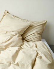 Beige Bettwäsche-Set auf einem Bett, bestehend aus einem Kissenbezug und einer Bettdecke, aus der Perspektive von oben fotografiert.