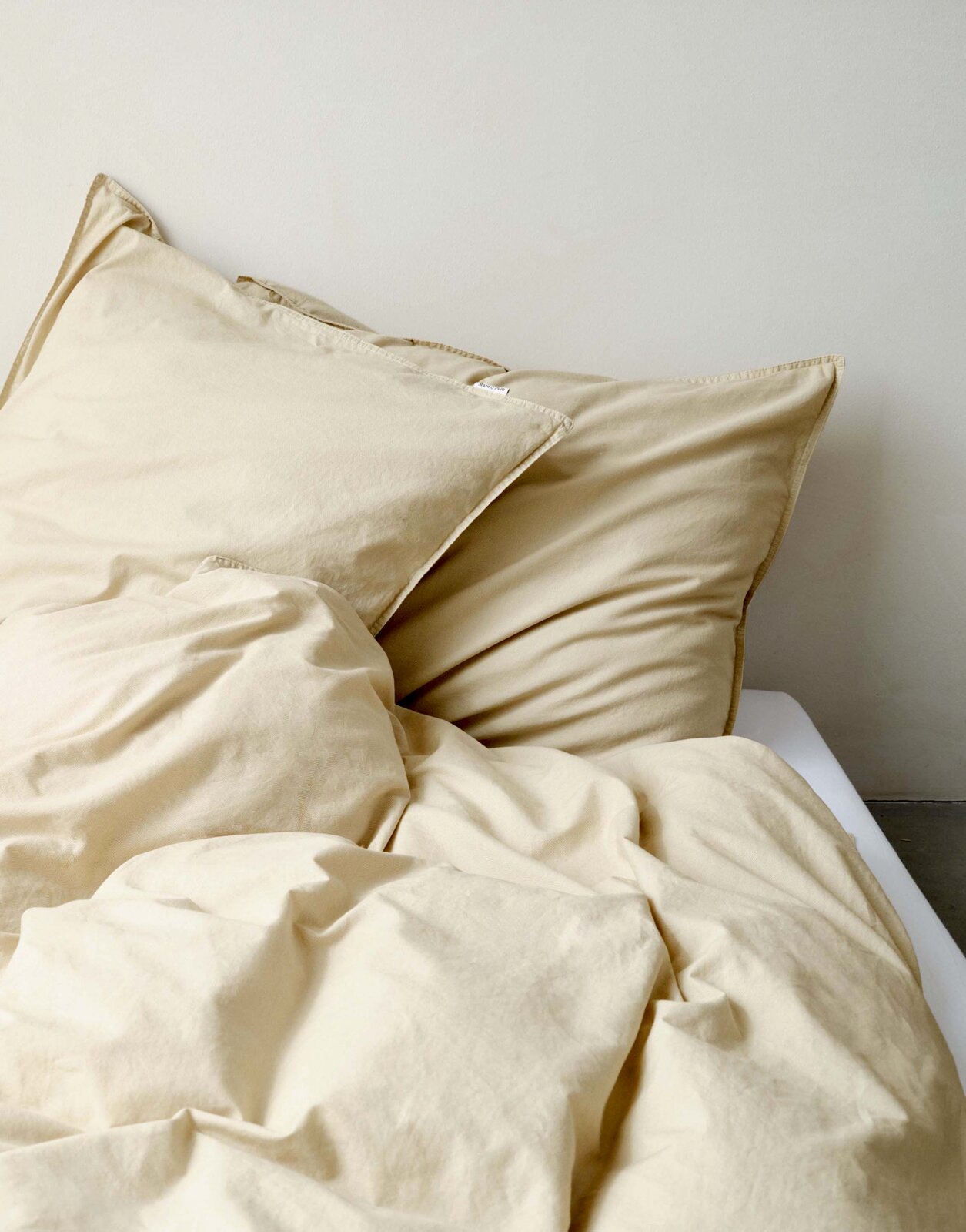 Beige Bettwäsche-Set auf einem Bett, bestehend aus einem Kissenbezug und einer Bettdecke, aus der Perspektive von oben fotografiert.