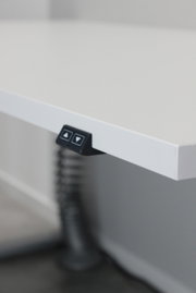 Nahaufnahme eines weißen E-Schreibtischs mit Bedienelementen an der Kante, seitliche Perspektive