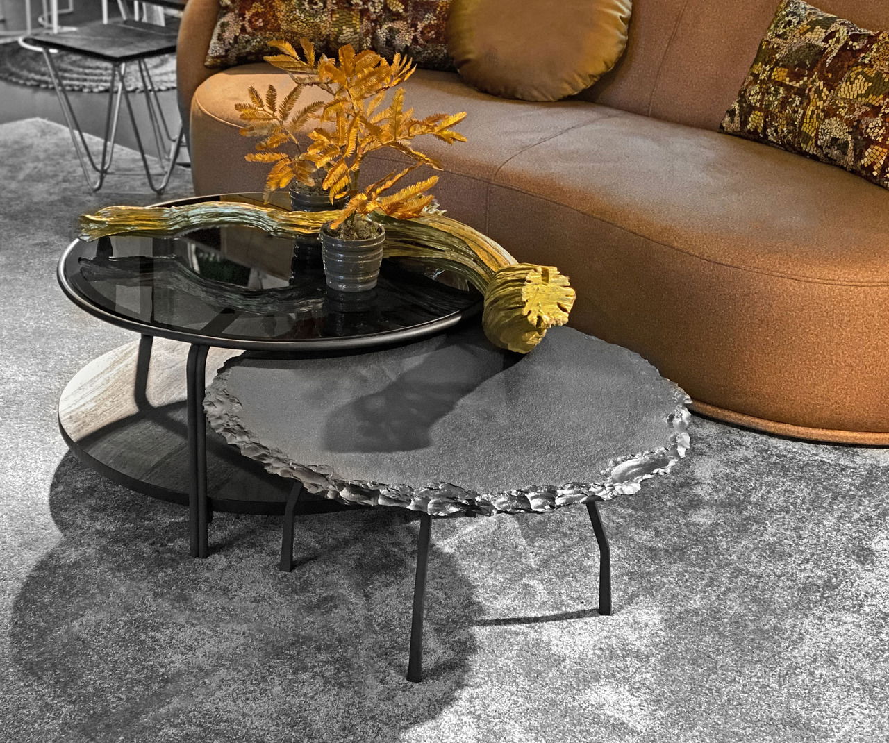 Zwei moderne Couchtische in einem Wohnzimmer, einer mit schwarzer Glasplatte und der andere mit unregelmäßiger Steinoptik, aus seitlicher Perspektive fotografiert.
