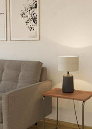 Tischleuchte CAPALBIO auf einem Holztisch neben einem grauen Sofa, seitliche Perspektive