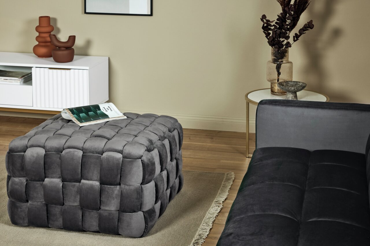 Jahnke Kruk WEB ART Grijze, gestoffeerde poef in een moderne woonkamer, zijaanzicht