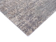 Designer Teppich in Grau- und Beigetönen mit abstraktem Muster, perspektivisch von der Seite fotografiert.