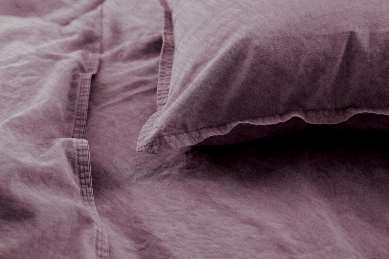 Nahaufnahme von lila Bettwäsche mit Kissenbezug, aus der Vogelperspektive fotografiert.