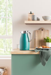Isolierkanne Skyline in Türkis auf einer Küchenarbeitsplatte, umgeben von Geschirr und Pflanzen, seitliche Perspektive