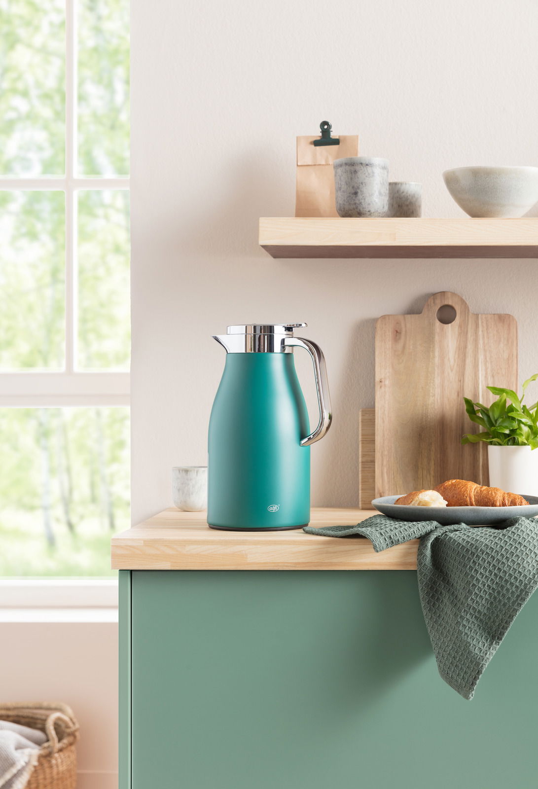 Isolierkanne Skyline in Türkis auf einer Küchenarbeitsplatte, umgeben von Geschirr und Pflanzen, seitliche Perspektive