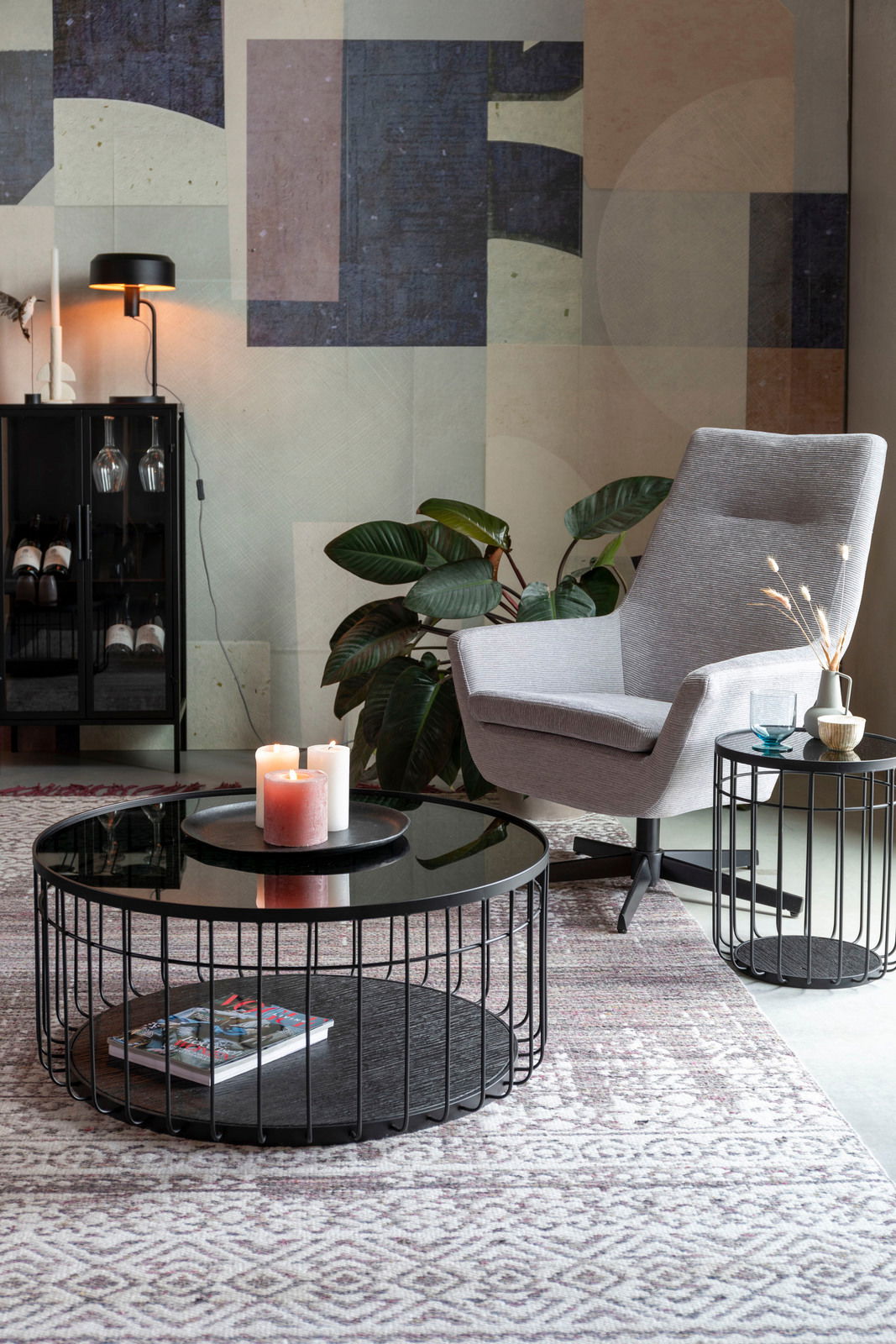 Moderner Couchtisch mit schwarzer Glasplatte und Metallgestell, frontal fotografiert, dekoriert mit Kerzen und Zeitschrift.