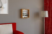 Frontale Ansicht einer an der Wand montierten Vitrine aus hellem Holz mit Glas-Schiebetüren, gefüllt mit Modellautos, im Wohnzimmer neben Stehlampe und rotem Vorhang.
