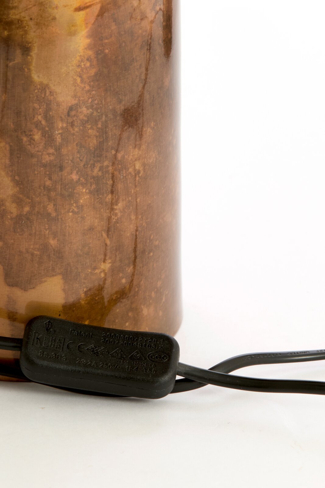 Detailaanzicht van de onderzijde van een cilindervormige lamp met bruin gemêleerde afwerking, zwart snoer en geïntegreerde snoerschakelaar, schuin van voren gefotografeerd