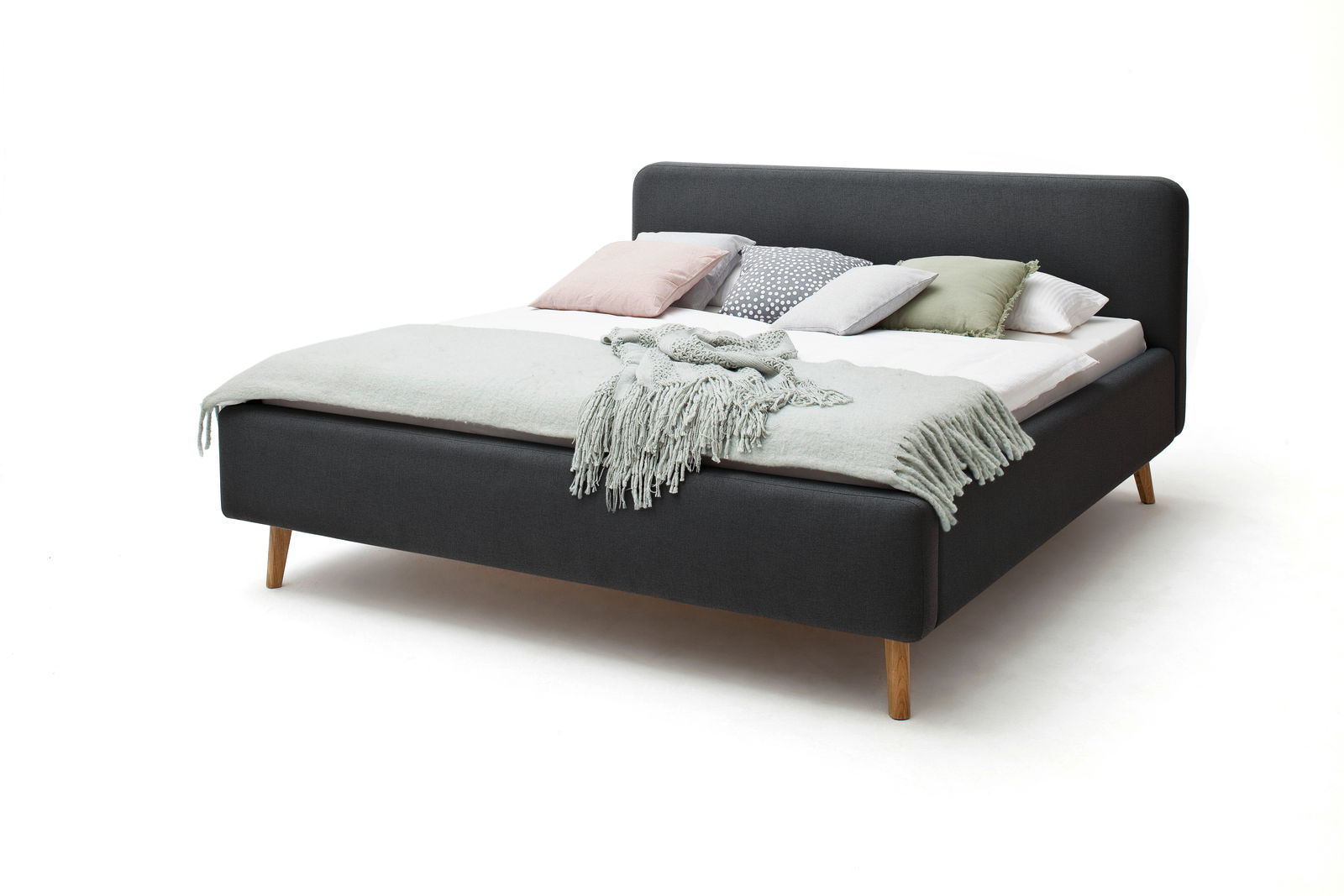 Polsterbett in Dunkelgrau mit Holzfüßen, dekoriert mit Kissen und einer Decke, seitliche Perspektive