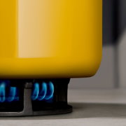 Gelber Topf auf einem Gasherd mit blauer Flamme, seitliche Perspektive