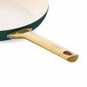 Nahaufnahme einer Bratpfanne mit goldfarbenem Griff und cremefarbener Innenbeschichtung, seitliche Perspektive