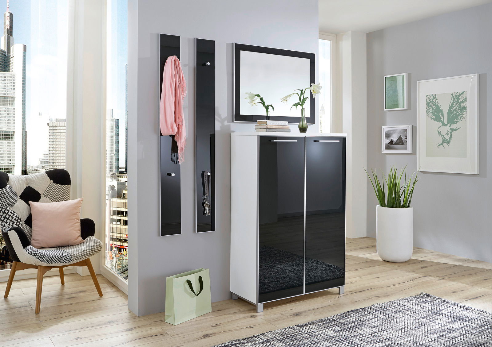 Modernes Garderoben-Set in einem hellen Raum mit Stadtblick, bestehend aus einem weißen Schrank mit schwarzen Hochglanztüren, zwei schmalen Wandpaneelen mit Haken und einem großen Spiegel darüber. Perspektive von vorne.
