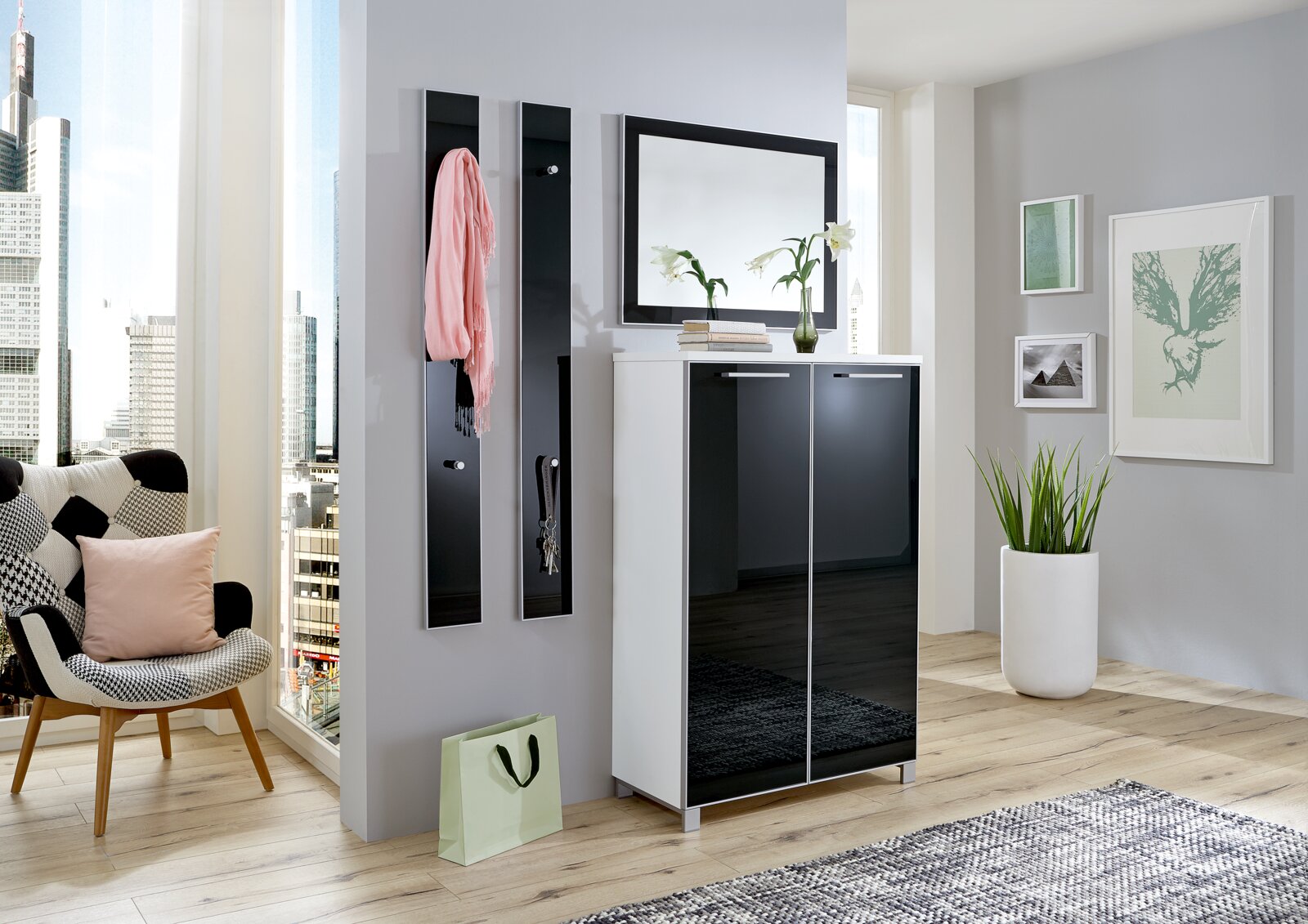 VOSS Garderoben-Set 4-tlg. SANTINA Modernes Garderoben-Set in einem hellen Raum mit Stadtblick, bestehend aus einem weißen Schrank mit schwarzen Hochglanztüren, zwei schmalen Wandpaneelen mit Haken und einem großen Spiegel darüber. Perspektive von vorne.